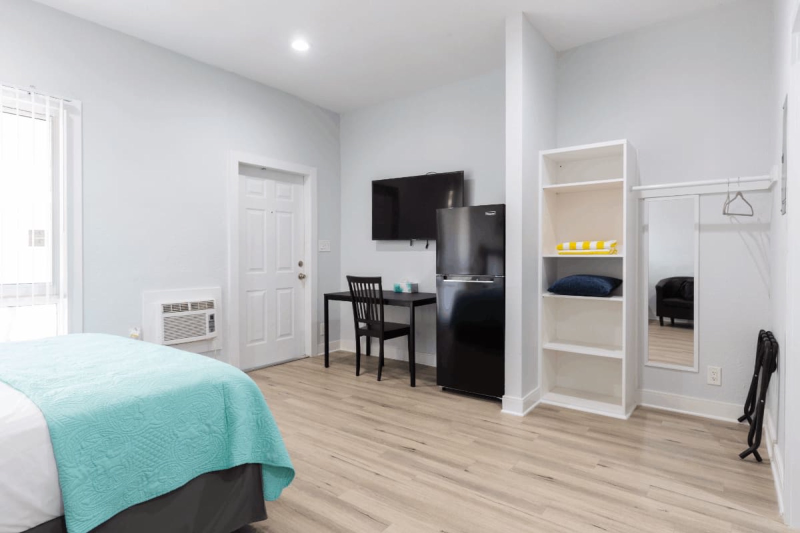 Studio with teal bedspread, fridge, shelving at Pompano Breeze, Pompano Beach