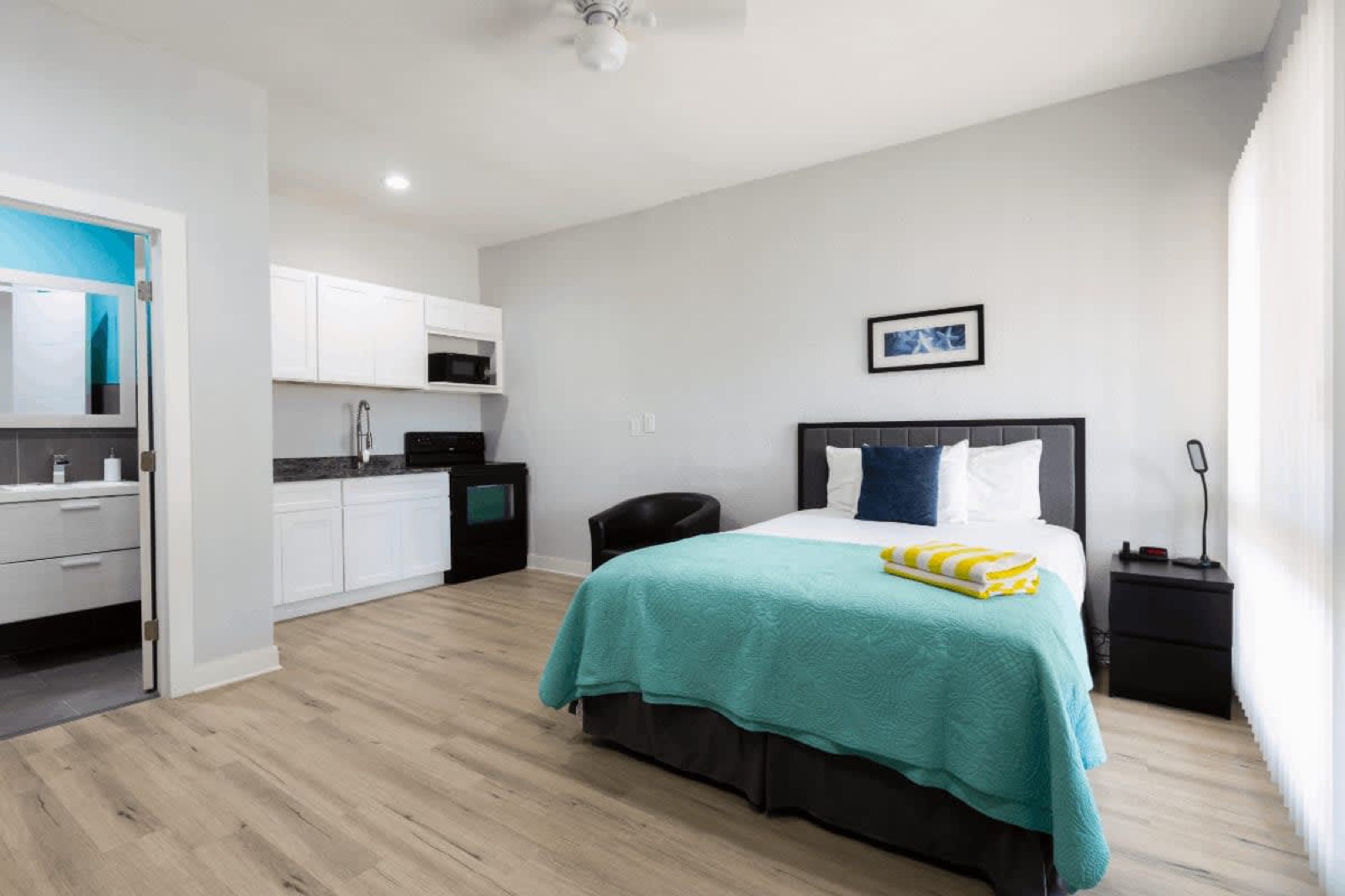 Studio bedroom with kitchenette and teal bedspread at Pompano Breeze, Pompano Beach