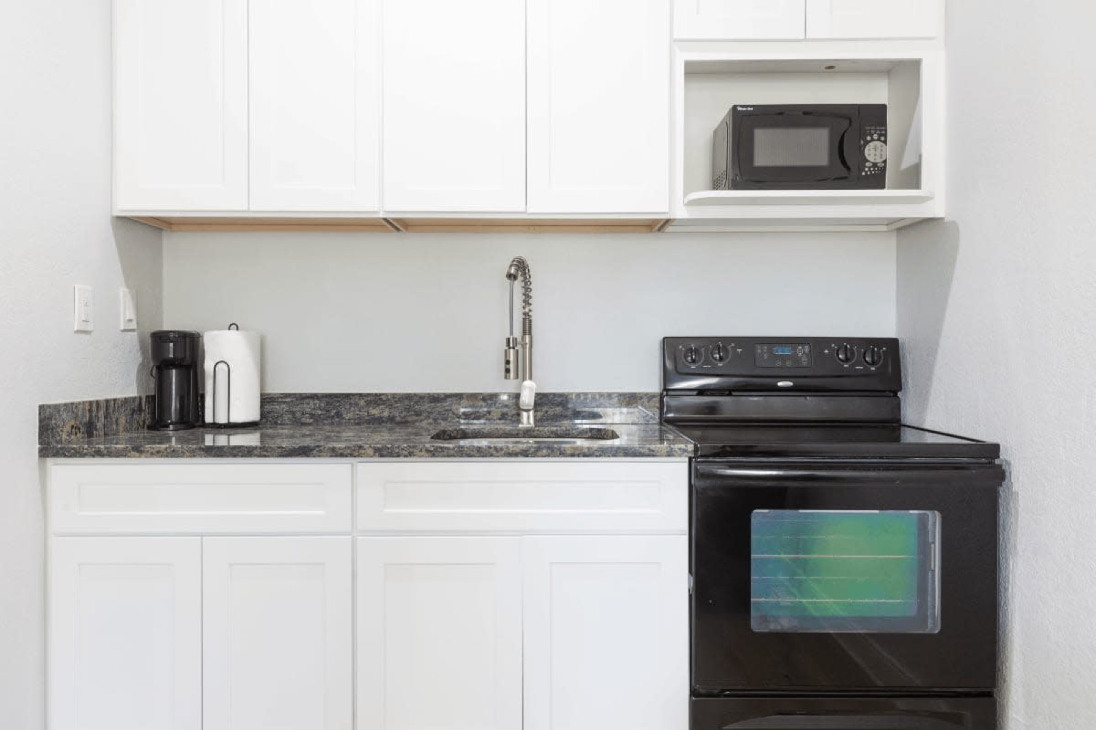 White kitchenette with black stove and microwave at Pompano Breeze, Pompano Beach