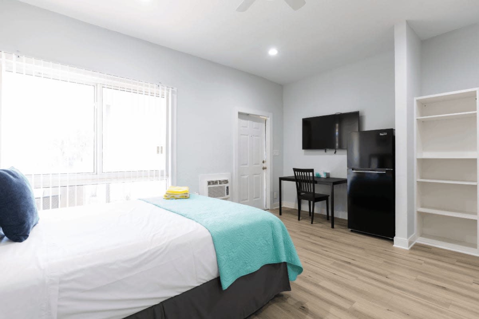 Studio bed with teal bedspread near window at Pompano Breeze, Pompano Beach