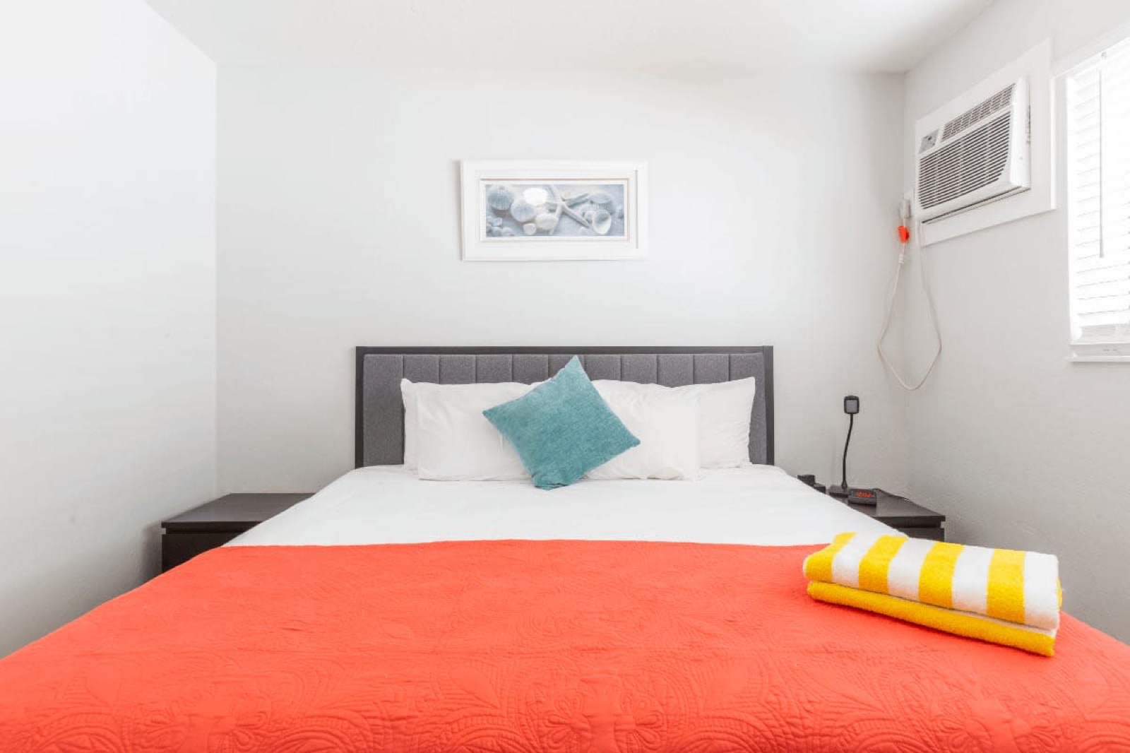 Bedroom with red bedspread and striped towels at Pompano Breeze, Pompano Beach